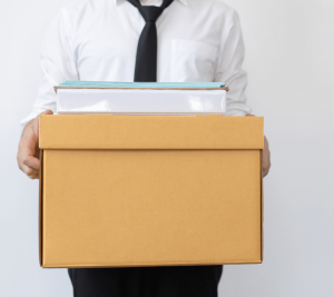 Pictured: A professional carrying a box of office items, as if they have packed up their office. This professional may rely on unemployment benefits after being let go.