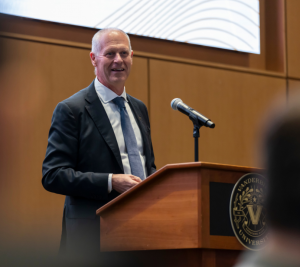 Pictured: Dean Steenburgh is standing at a podium in front of a microphone.